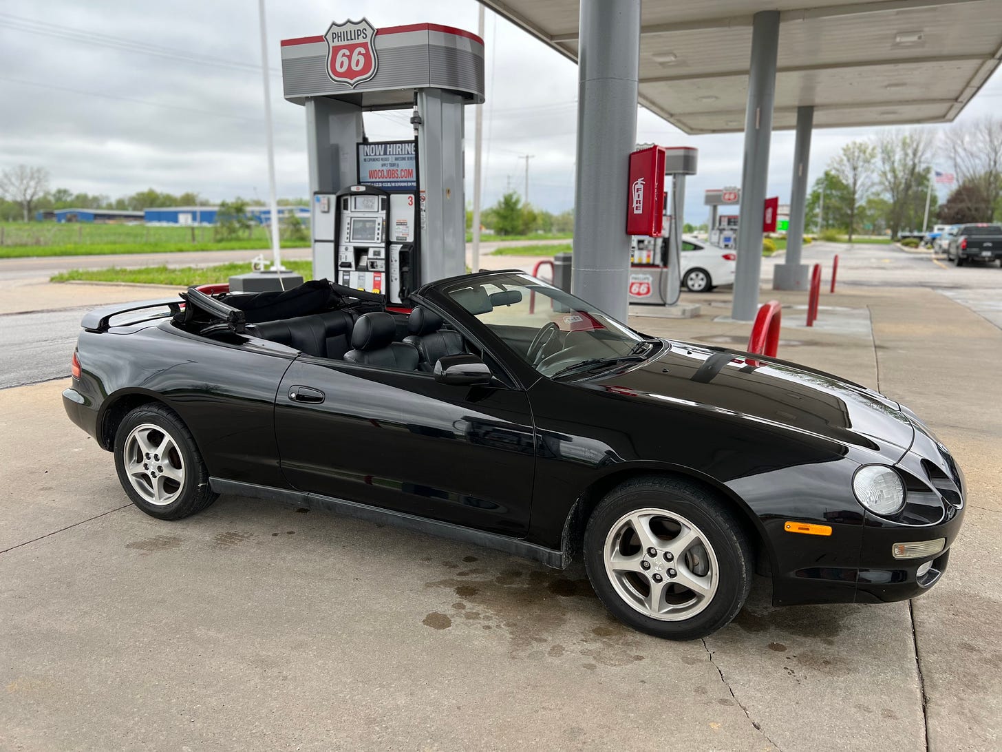 A black convertible at a gas pump. It's a pretty fucking cool looking car.