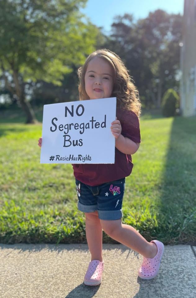 [image] Rosie, a young girl with Down syndrome holds a sign; text reads: NO Segregated Bus #RosieHasRights