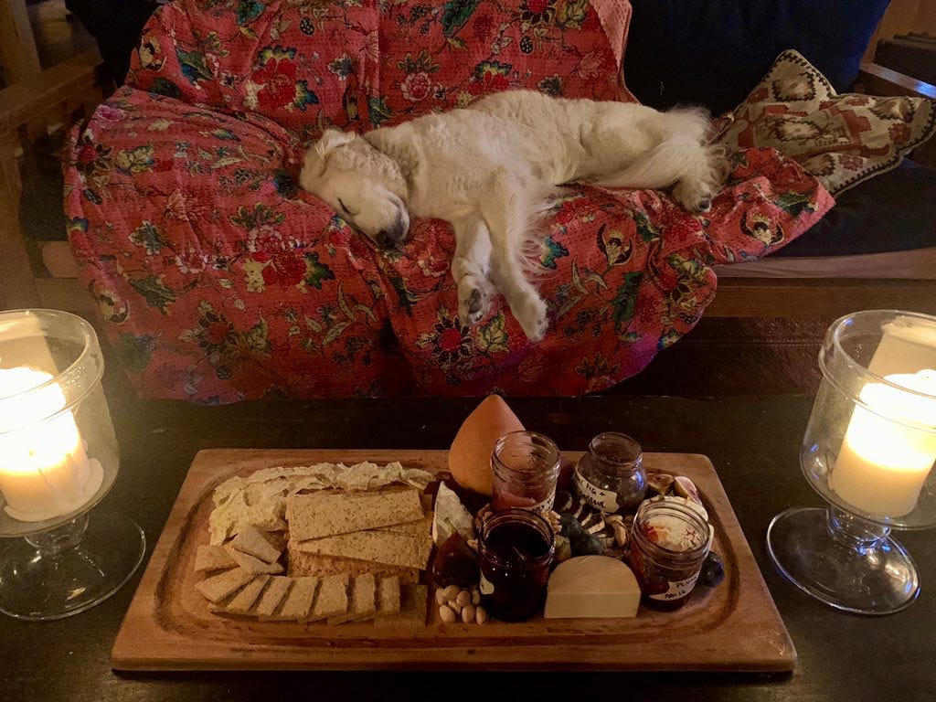 a dog sleeps on a couch in front of a table with a large cheese plate and candles