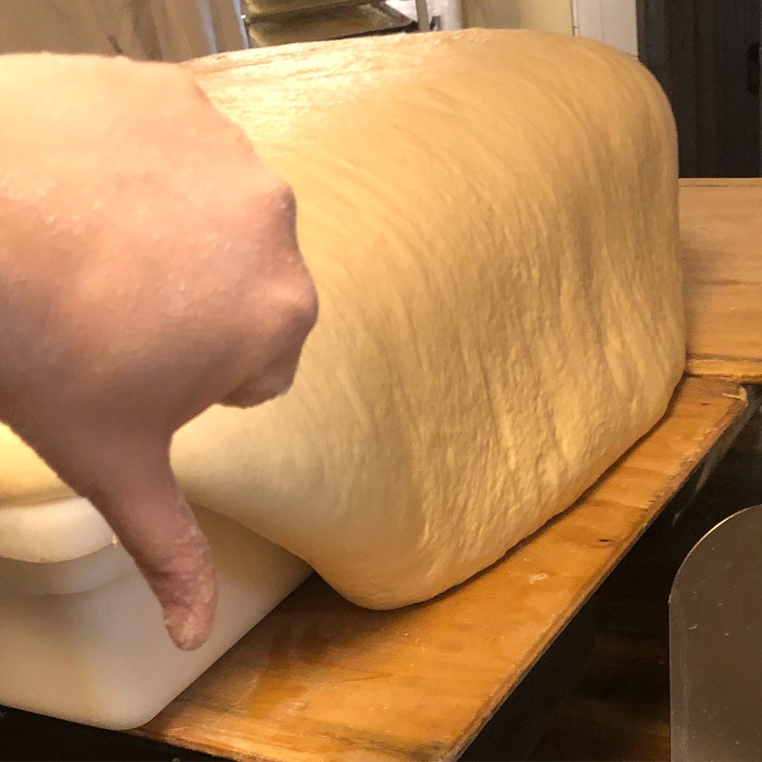 A tub of overflowing dough with a hand giving a thumbs down in the foreground.