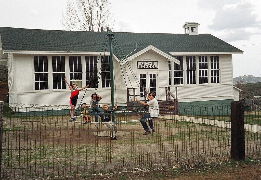 Kids playing on swinging merry-go-round in front of the Midas School in Midas, Nevada, 2004. The one-room schoolhouse was built 1927 and closed in 1972 as rural Nevada populations shrunk.