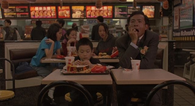 A Chinese man yawns in a McDonalds while his son eats a meal