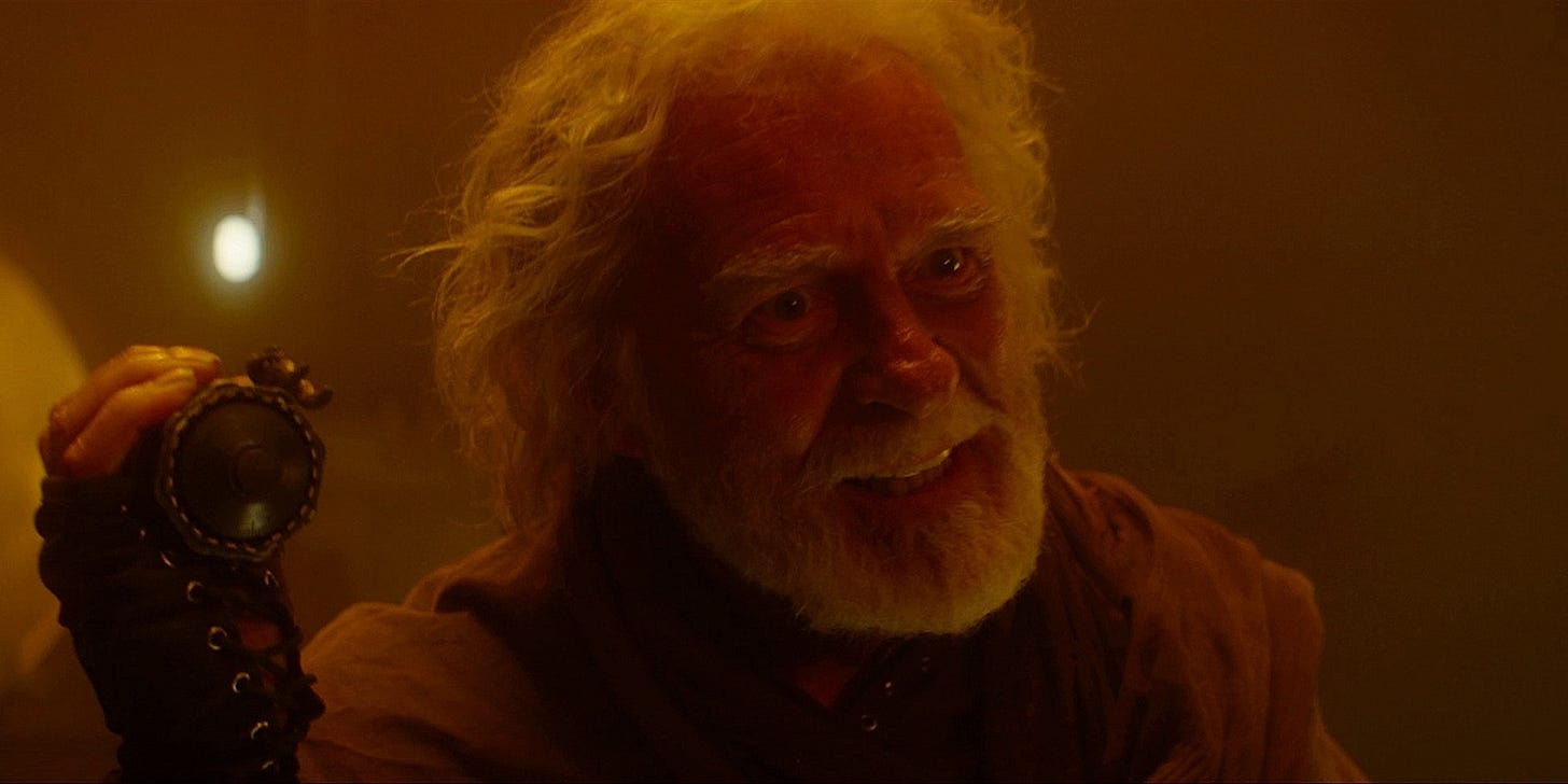 This image shows the character Ko Sharmus (played by Ian McElhinney) holding the Death Particle detonator just before he activates this device. Sharmus confronts the offscreen Master with a smile on his face and a glint in his eye before sacrificing his life to save the universe from the Cyberman threat. This image shows the character Ko Sharmus (played by Ian McElhinney) holding the Death Particle detonator just before he activates this device. Sharmus confronts the offscreen Master with a smile on his face and a glint in his eye before sacrificing his life to save the universe from the Cyberman threat.