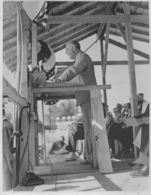 Man standing at wooden podium on covered outdoor stage