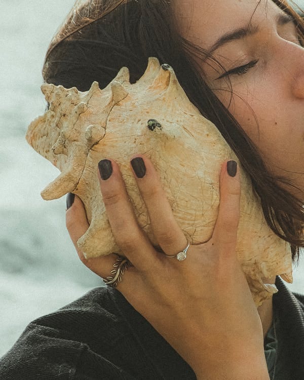 Free A Woman Holding White Sea Shell Near Her Ear Stock Photo