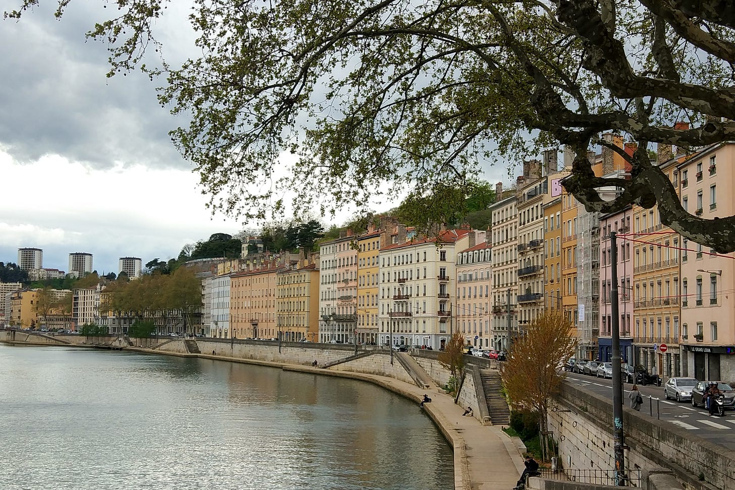 Pastel-toned buildings alongside the Soane river in Lyon, on a cloudy day.