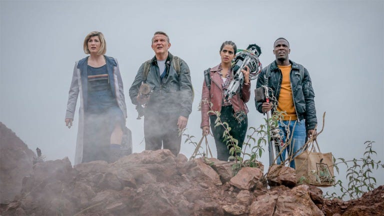 This image shows, from left to right, the Thirteenth Doctor (played by Jodie Whittaker), Graham O’Brien (played by Bradley Walsh), Yasmin “Yaz” Khan (played by Mandip Gill), and Ryan Sinclair (played by Tosin Cole) standing on a ridge and looking offscreen at humanity's last outpost / settlement. Graham, Yaz, and Ryan carry equipment to be used in the encampment's defense. This image shows, from left to right, the Thirteenth Doctor (played by Jodie Whittaker), Graham O’Brien (played by Bradley Walsh), Yasmin “Yaz” Khan (played by Mandip Gill), and Ryan Sinclair (played by Tosin Cole) standing on a ridge and looking offscreen at humanity's last outpost / settlement. Graham, Yaz, and Ryan carry equipment to be used in the encampment's defense.