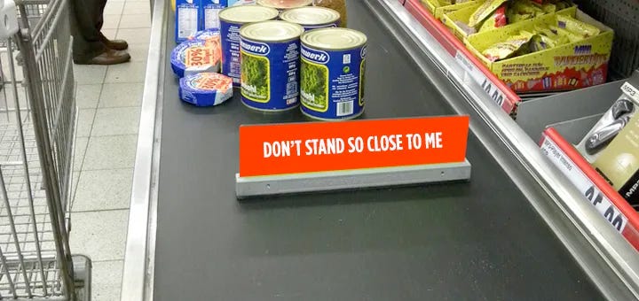 canned food on a grocery checkout ramp behind a sign that sayd "don't stand so close to me"
