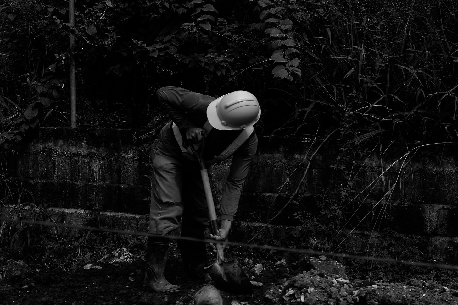 A man in a hard hat holds a spade in his hand, digging into the ground.