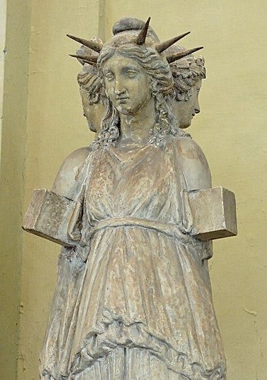 We see the upper part of an unpainted Roman stone copy of a Greek statue: three women standing back-to-back, their arms ending strangely in cubes right below the shoulder; the one facing the camera wears a spiked crown with no spike right over her brow.