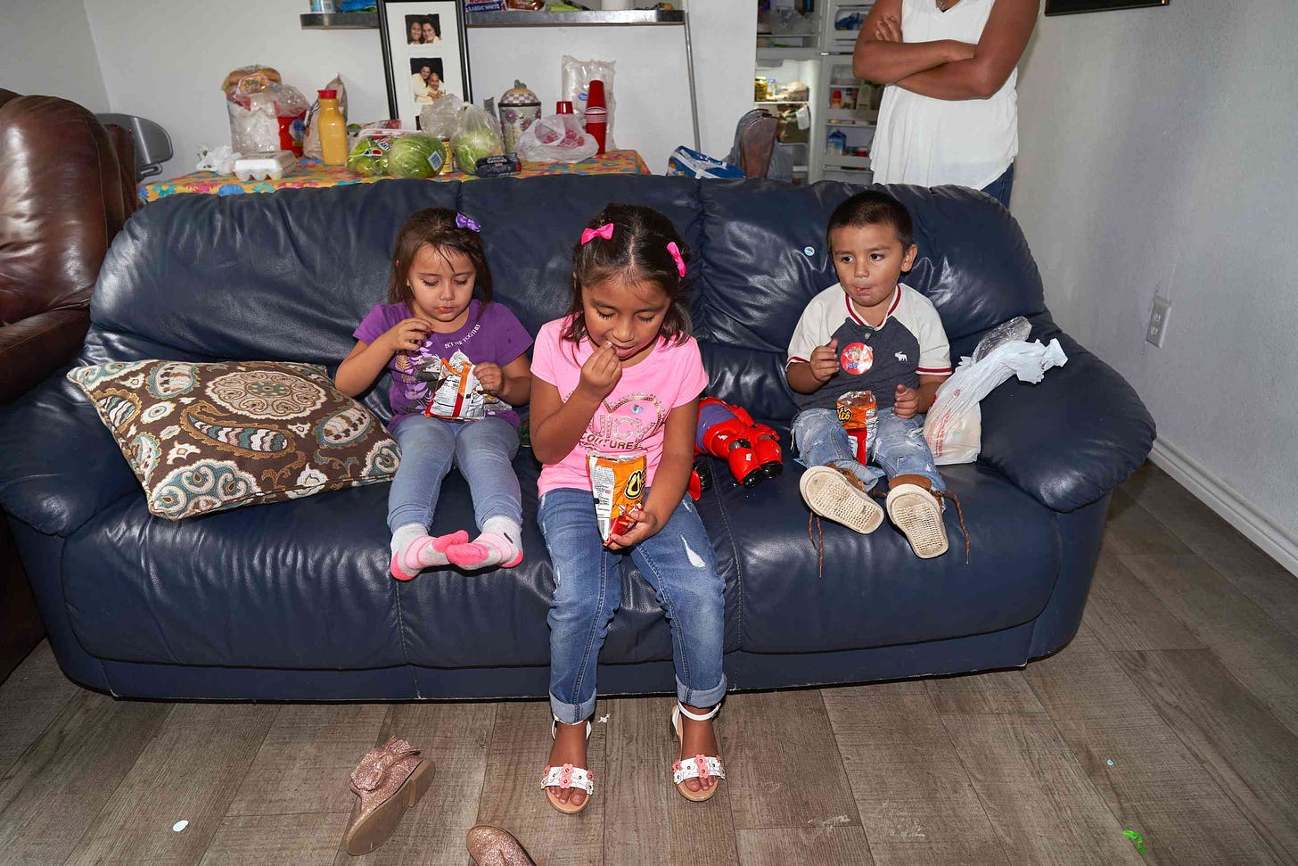 Rivera’s children eat Cheetos on the couch after returning home from picking up groceries. (From left: Destiny, 4, Ana, 6, Jonathan, 3.)