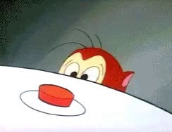 Cartoon Stimpy the cat looking concerned while peaking above an edge of a surface at a big red button in the foreground