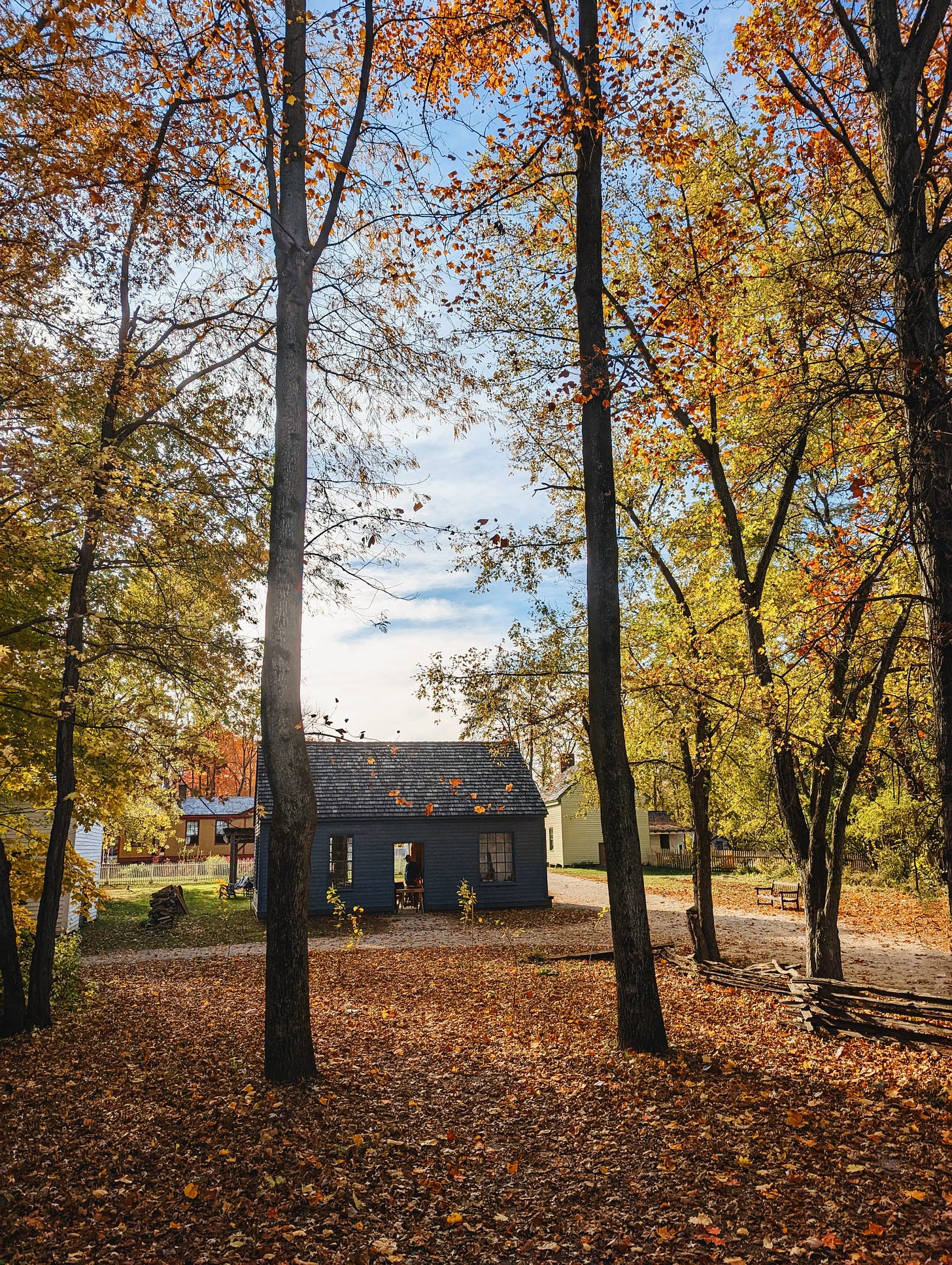 A small, blue building sits among autumn trees inside of Conner Prairie's living history museum.