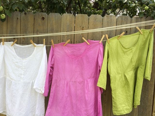 Three tunic tops on a clothesline. From left to right, they're white, pink, and green.