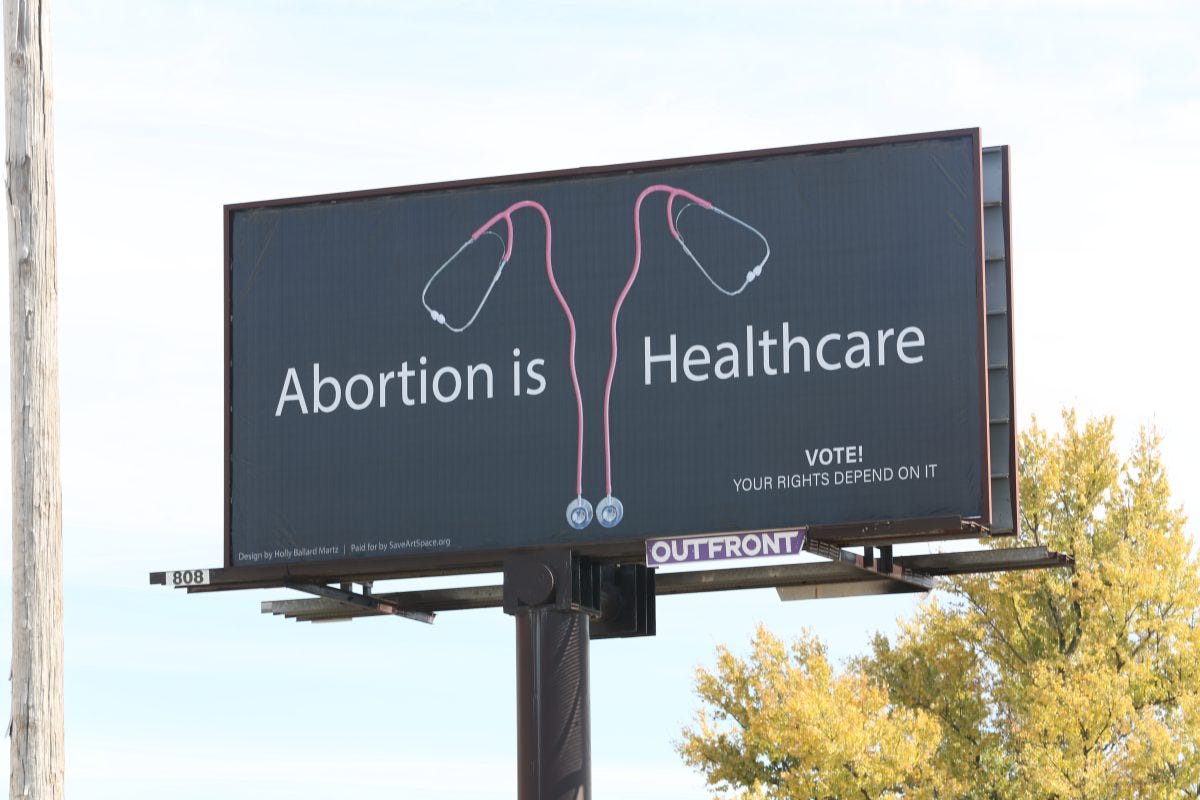 Billboard with pro-abortion message, reading 'Abortion is Healthcare' and 'Vote! Your Rights Depend on It' The image are two stethoscopes forming a woman's reproductive system on a black background.