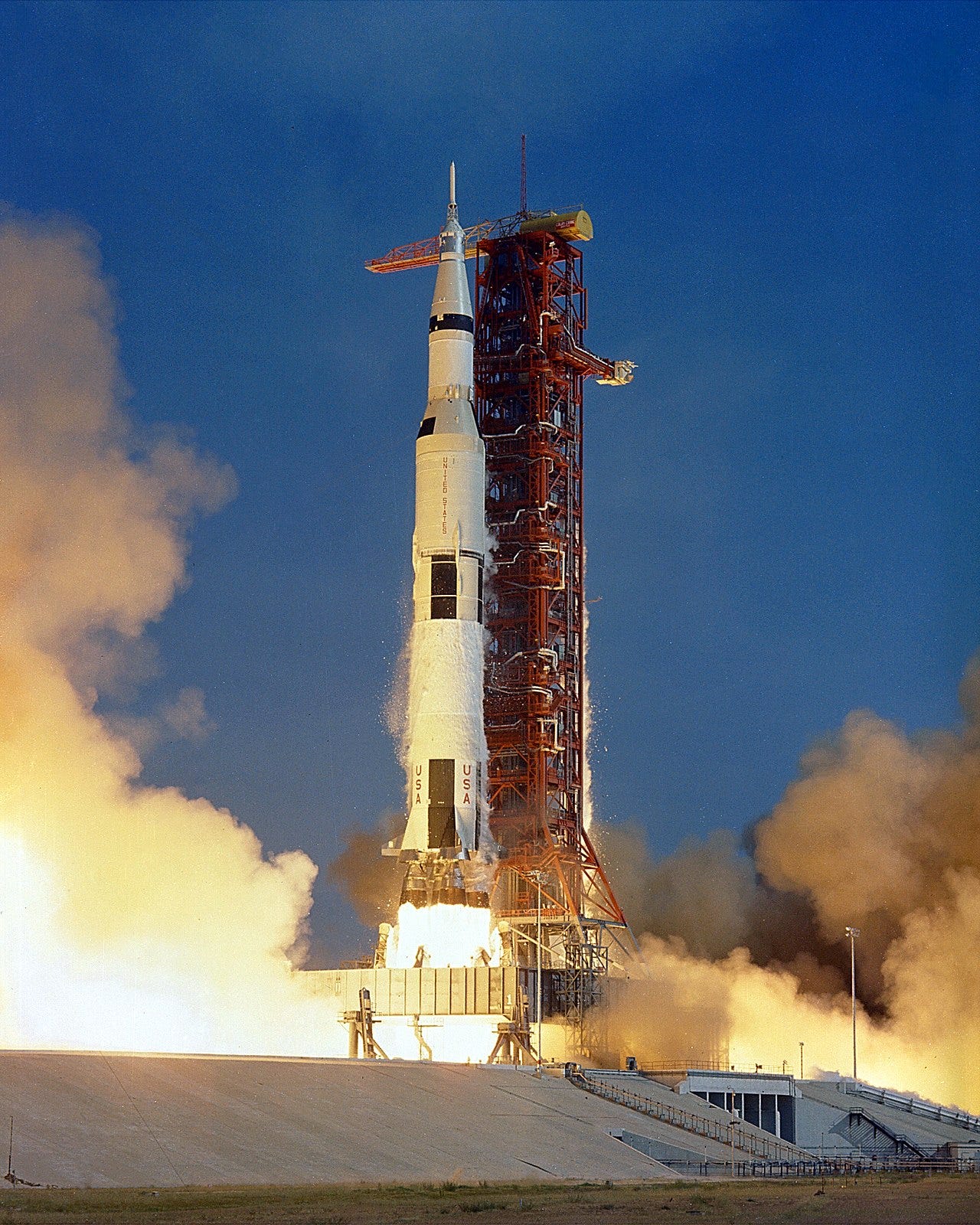 A Saturn V rocket with engines firing on the launch tower