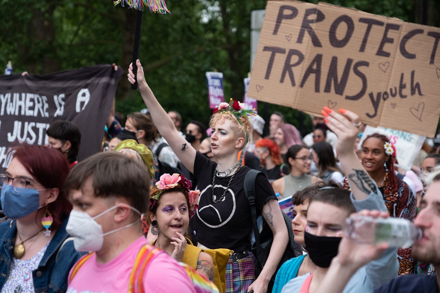 Photo of a trans rights protest in the UK. A cardboard sign in the top-right reads "PROTECT TRANS YOUTH"