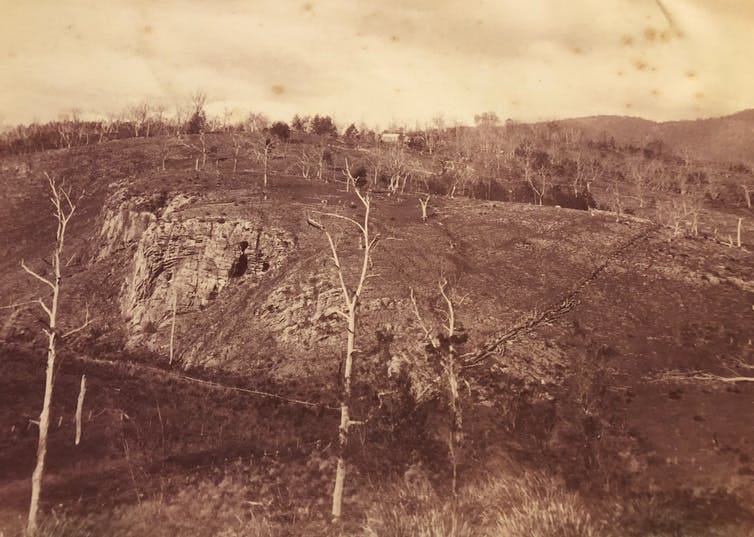 A thinly forested hill with a limestone formation and cave entrance in the middle-distance.