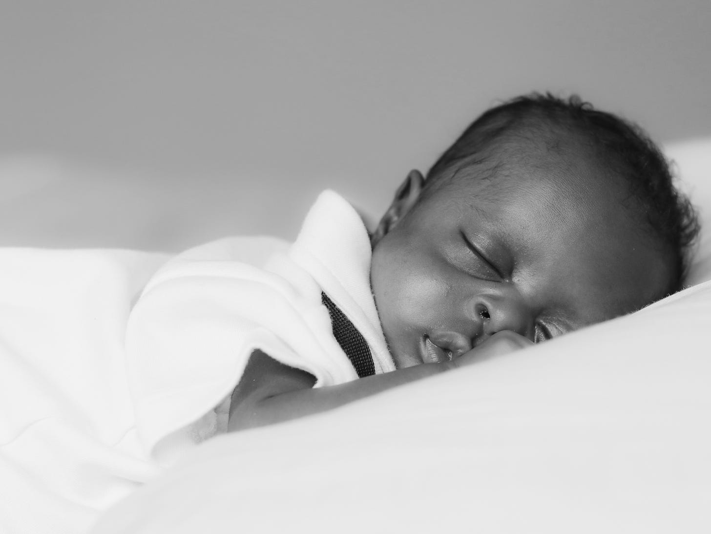 Infant sleeping on stomach on a white sheet and mattress