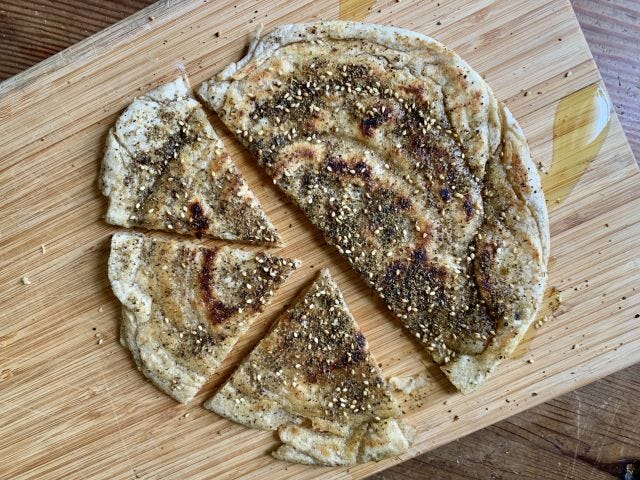 A pancake on a cutting board covered in za'atar, with triangular pieces cut out of it