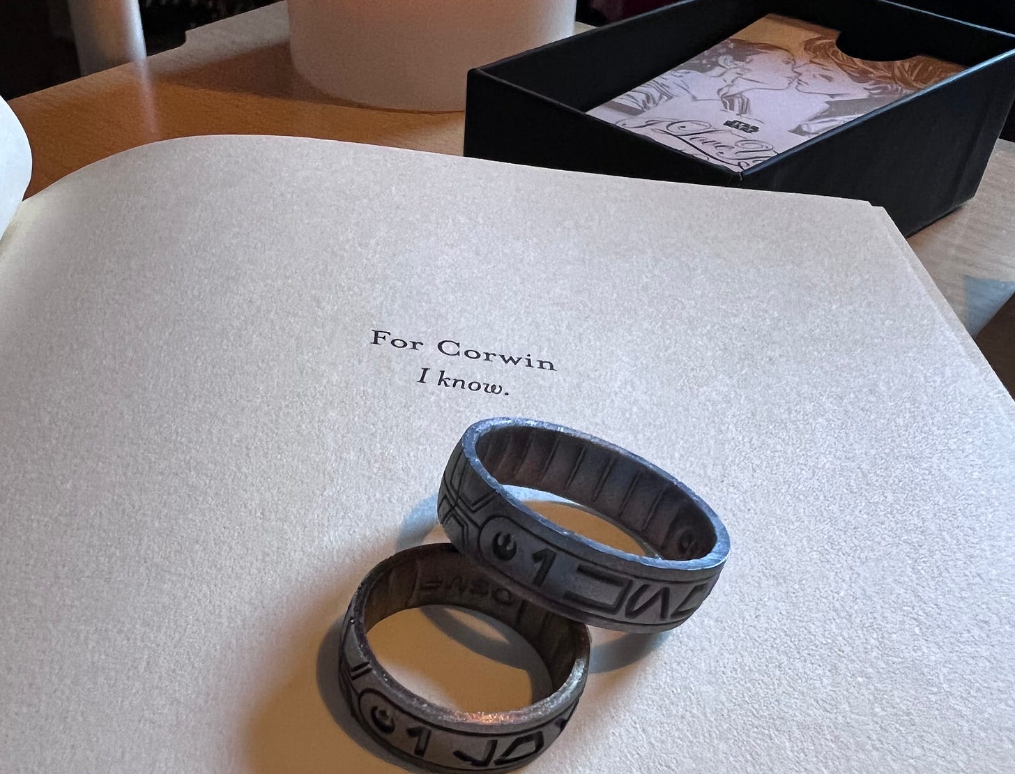 Photo of the dedication page of Rebel Rising and a pair of rings