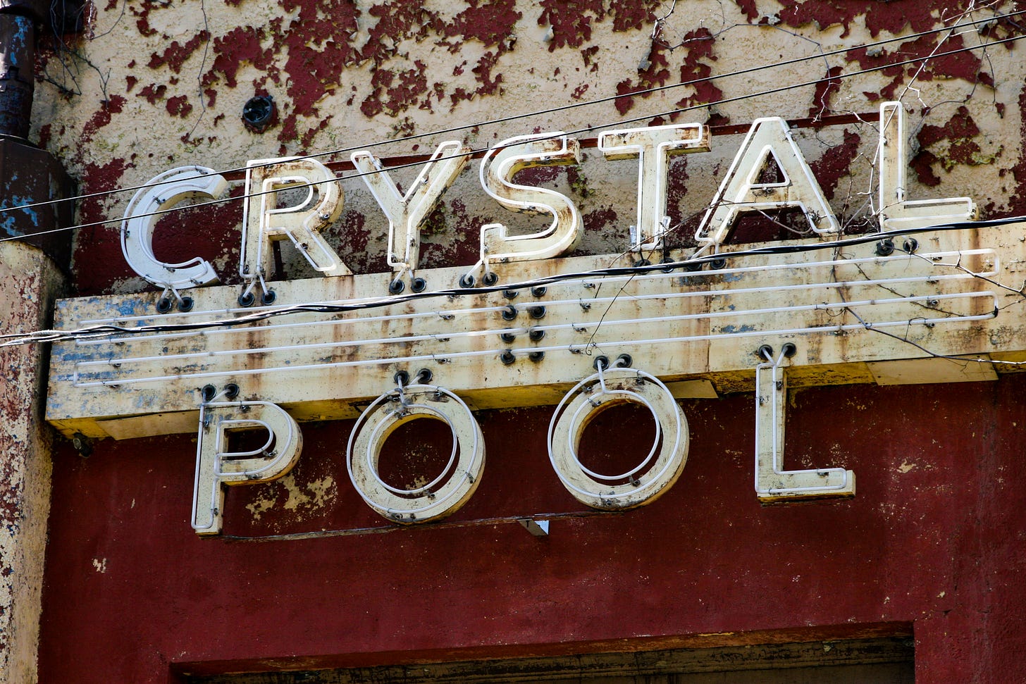 Crystal Pool neon sign on building with chippy dark red and beige paint