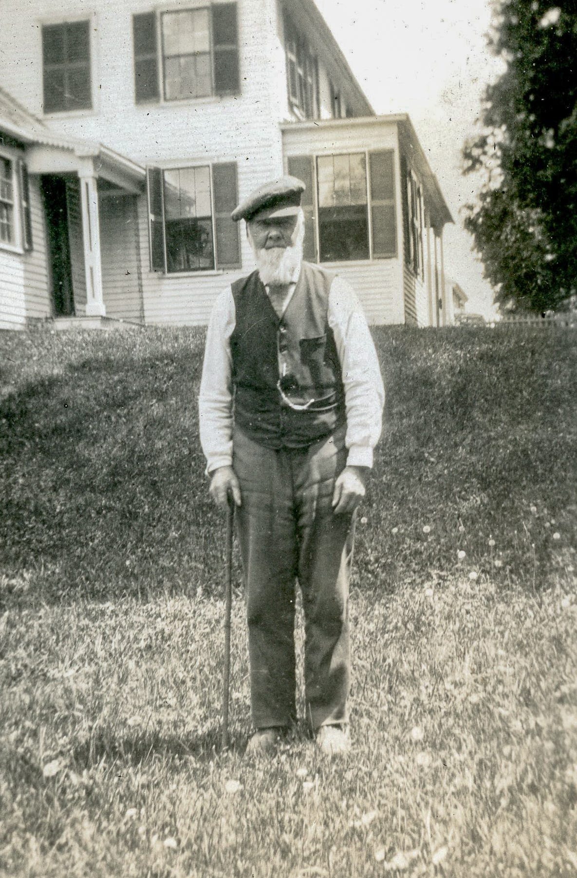 Bearded man with cane in front of house