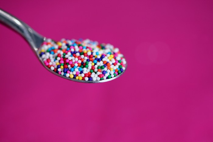 A spoon filled with dots on in the foreground with a pink background