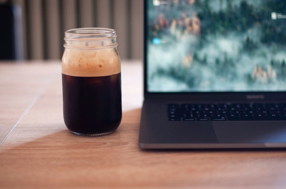 clear glass mason jar filled with black liquid beside turned-on laptop
