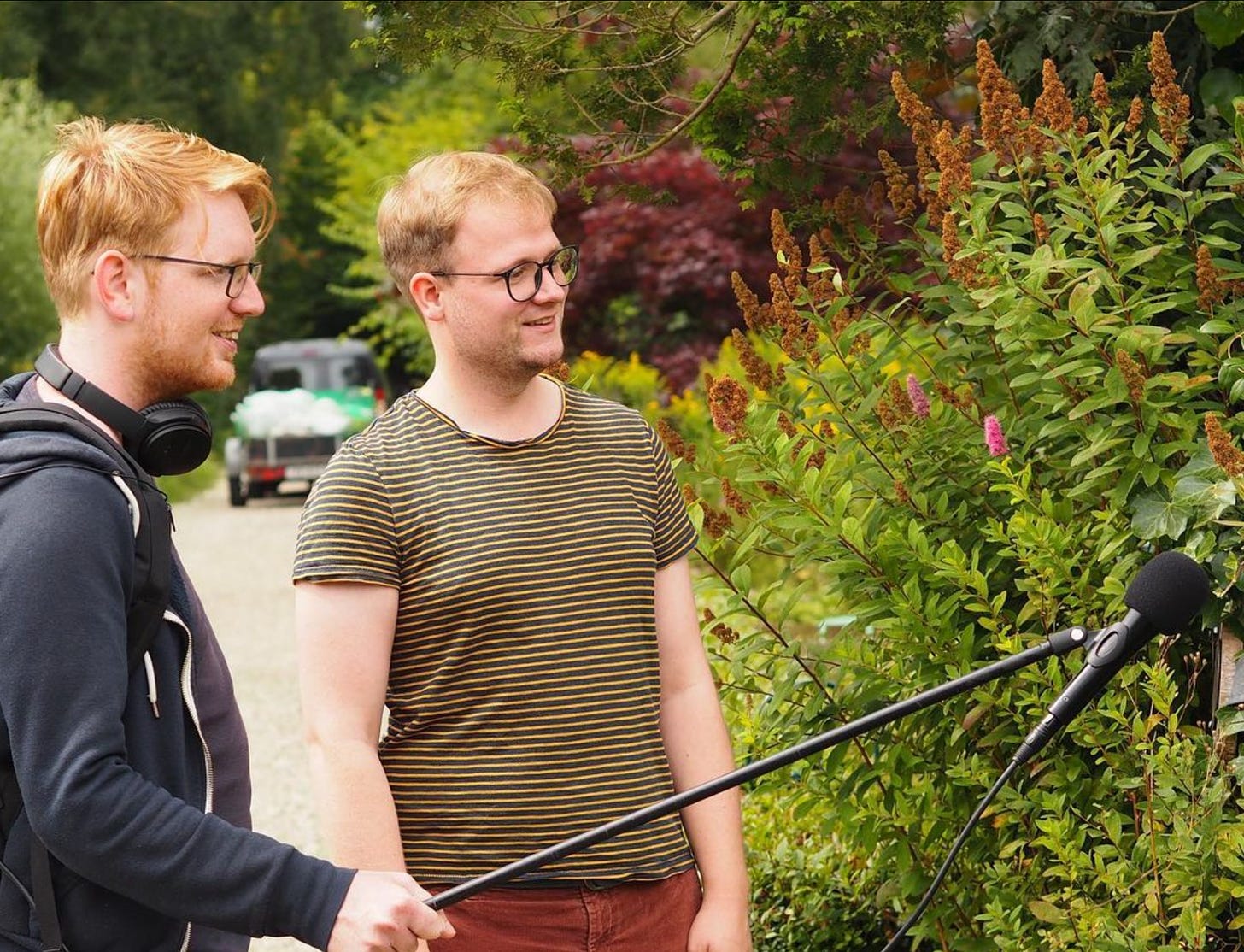 foto van Groentjes makers Marius (rood haar, bril) en Jurgen (Blond haar, ook bril) die in een tuin staan. Ze kijken naar buiten de foto een bosje in, Marius heeft een microfoon op een hengel vast waarmee hij het bosje lijkt te interviewen