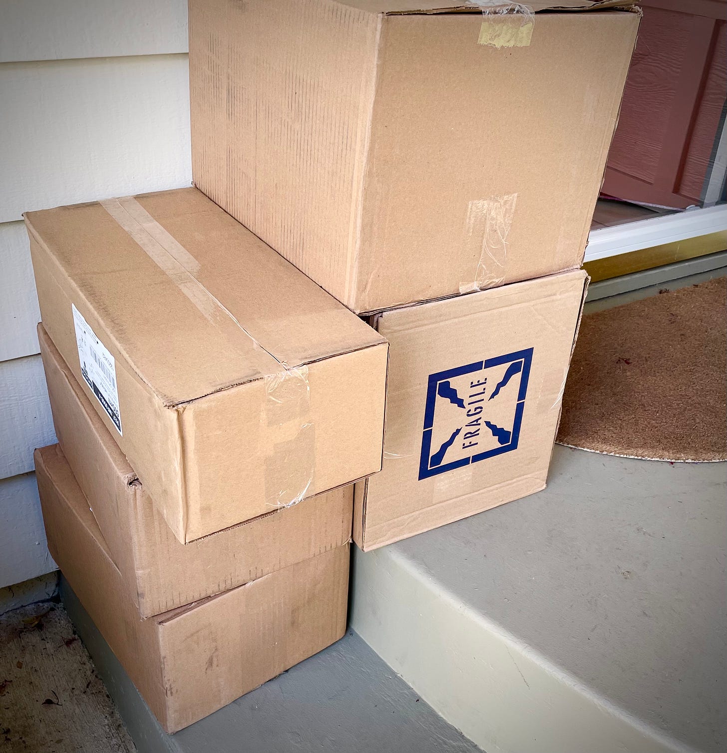A package marked "fragile" rests crooked under other packages on stairs in front of a door. 