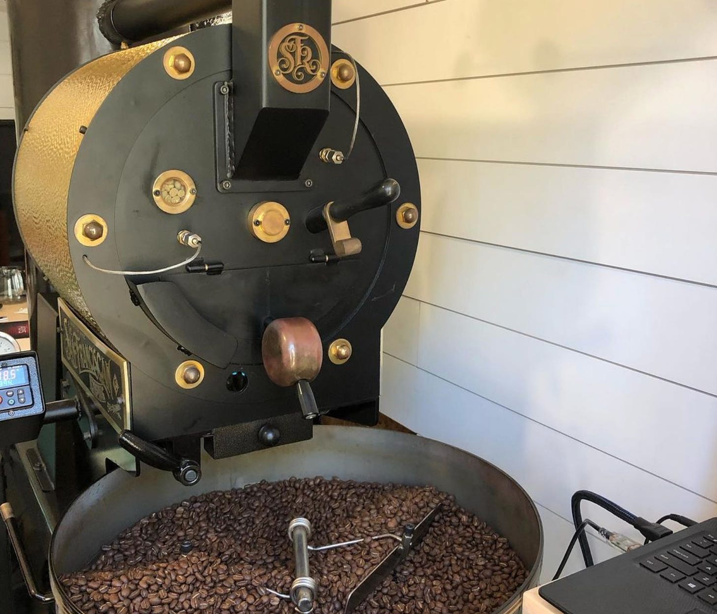 A retro industrial style looking commercial coffee roaster. A big drum is full of roasting coffee beans. 