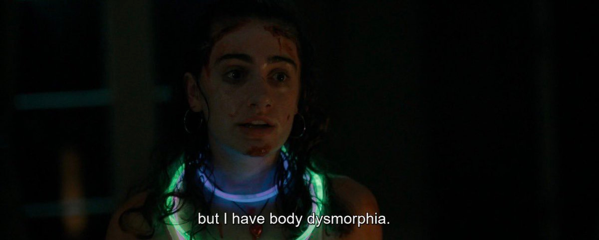 A close-up of a 20-something year old women wearing a glow-in-the-dark necklace. Her hair is wet and she has some blood on her face. Her caption reads "but I have body dysmorphia." The shot is from the movie Bodies Bodies Bodies.