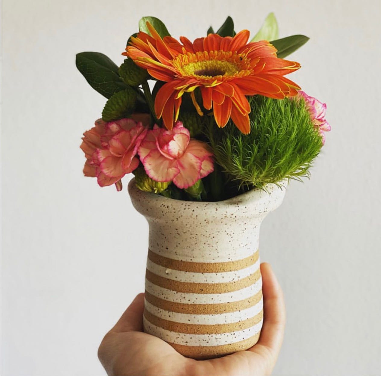 Small narrow flower pot made by Dr. Camacho. The flower pot is cream with light brown stripes at the base. The flower pot is holding a small colorful mix of flowers.