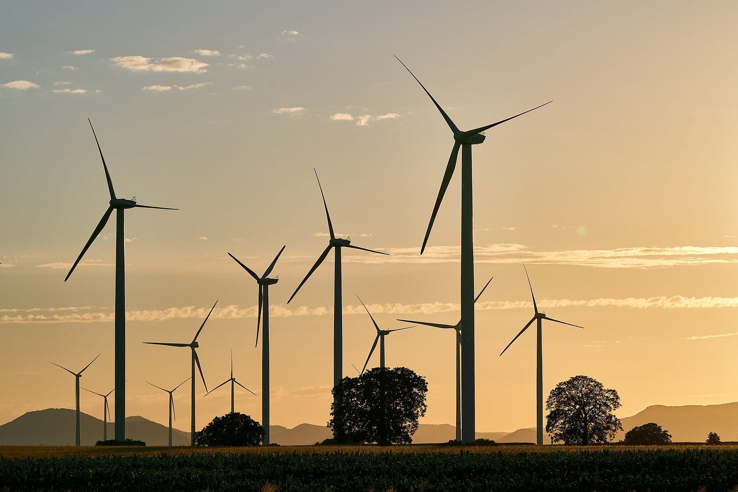 Wind turbines in an idyllic scene with mist on the ground and sunrise off the to right.