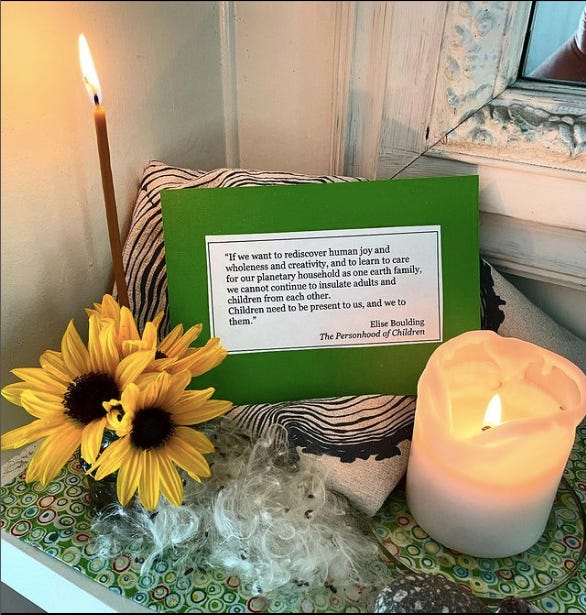 a personal altar including a green card with an Elise Boulding quote, two candles, sunflowers, and seeds