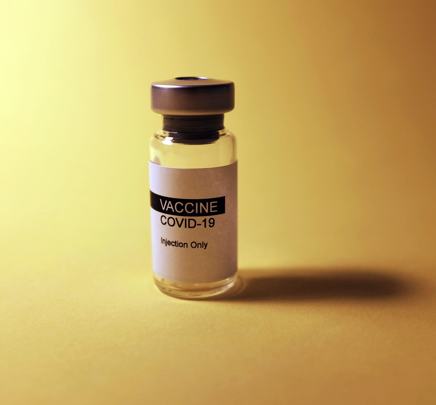 A glass vial labelled 'Vaccine Covid-19' with a light yellow background.