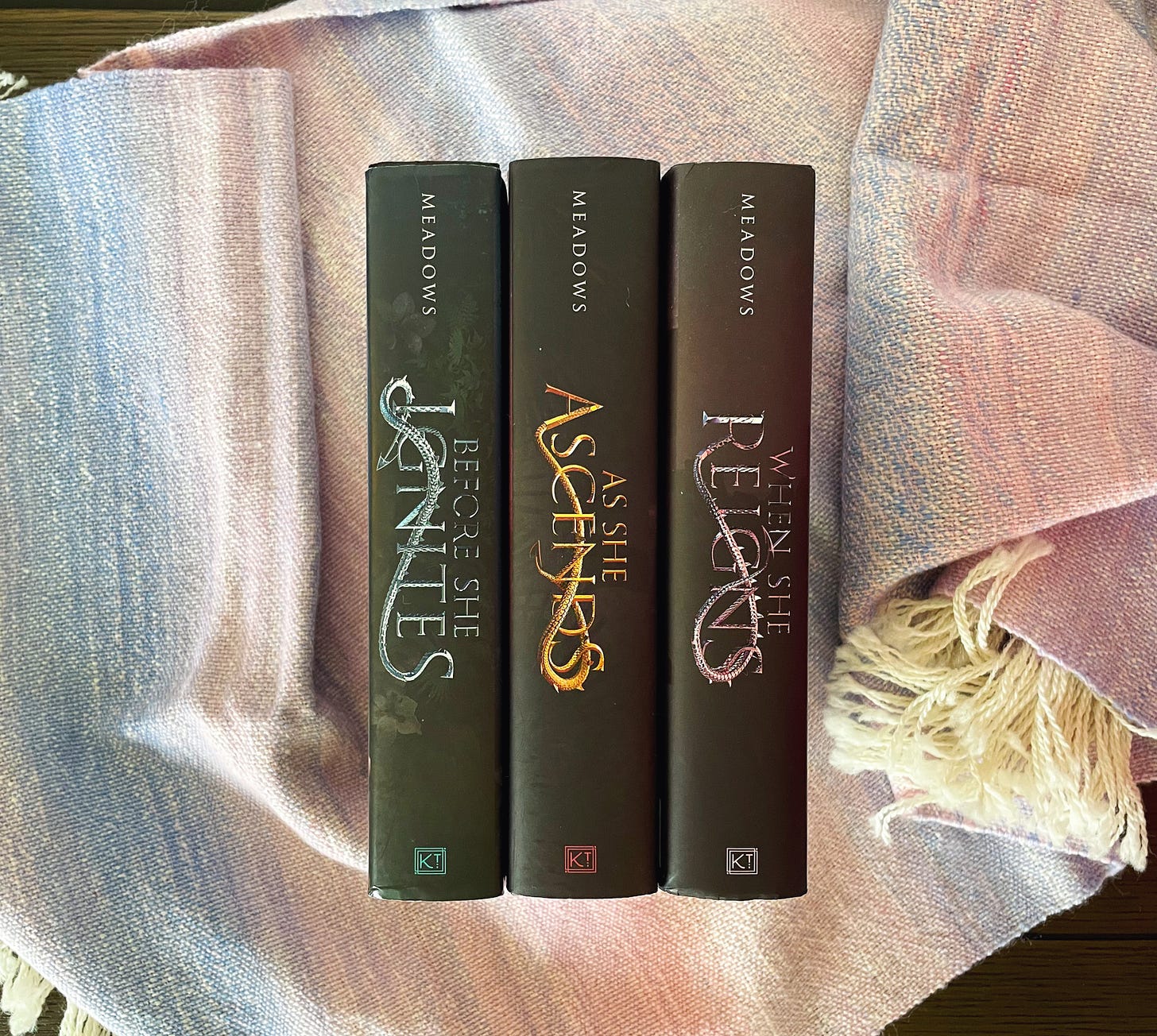 Three books, the Fallen Isles trilogy, on a pastel woven cloth