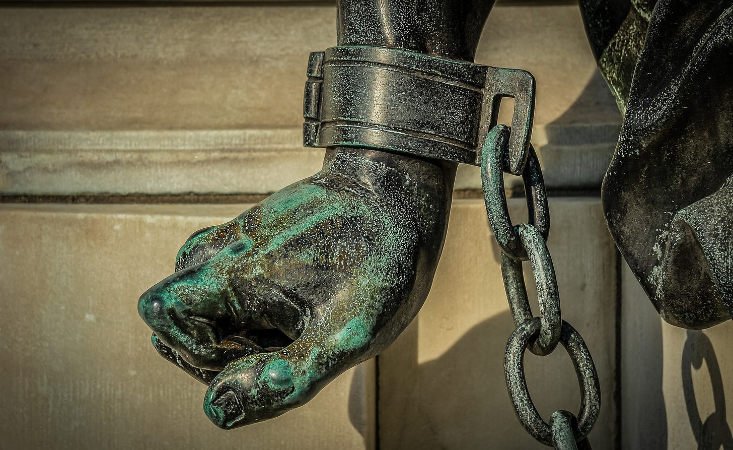 Image of statute, closeup of hand, in cuff and chains.