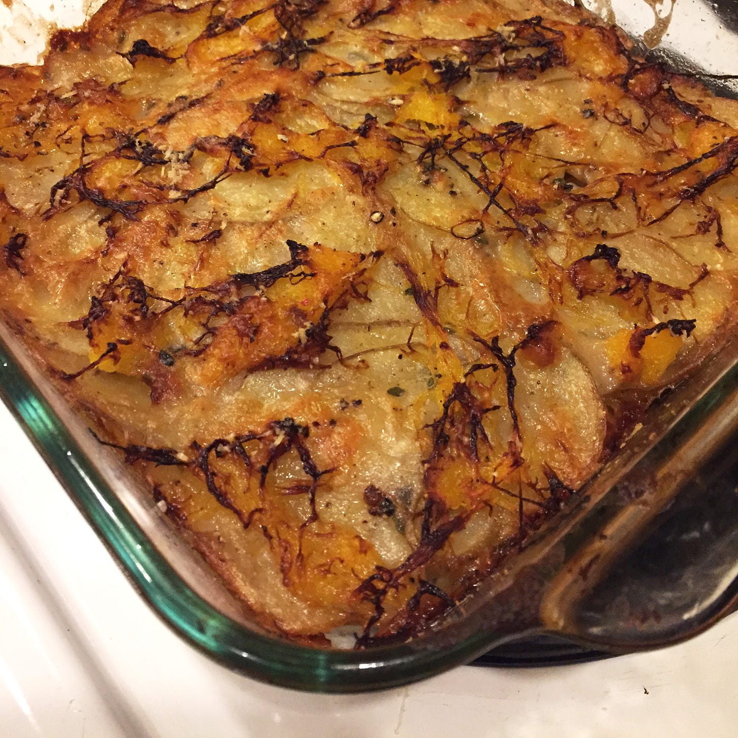 a square Pyrex pan full of a gratin made of thinly sliced potatoes and spaghetti squash. The top is charred in places and the edges have browned.