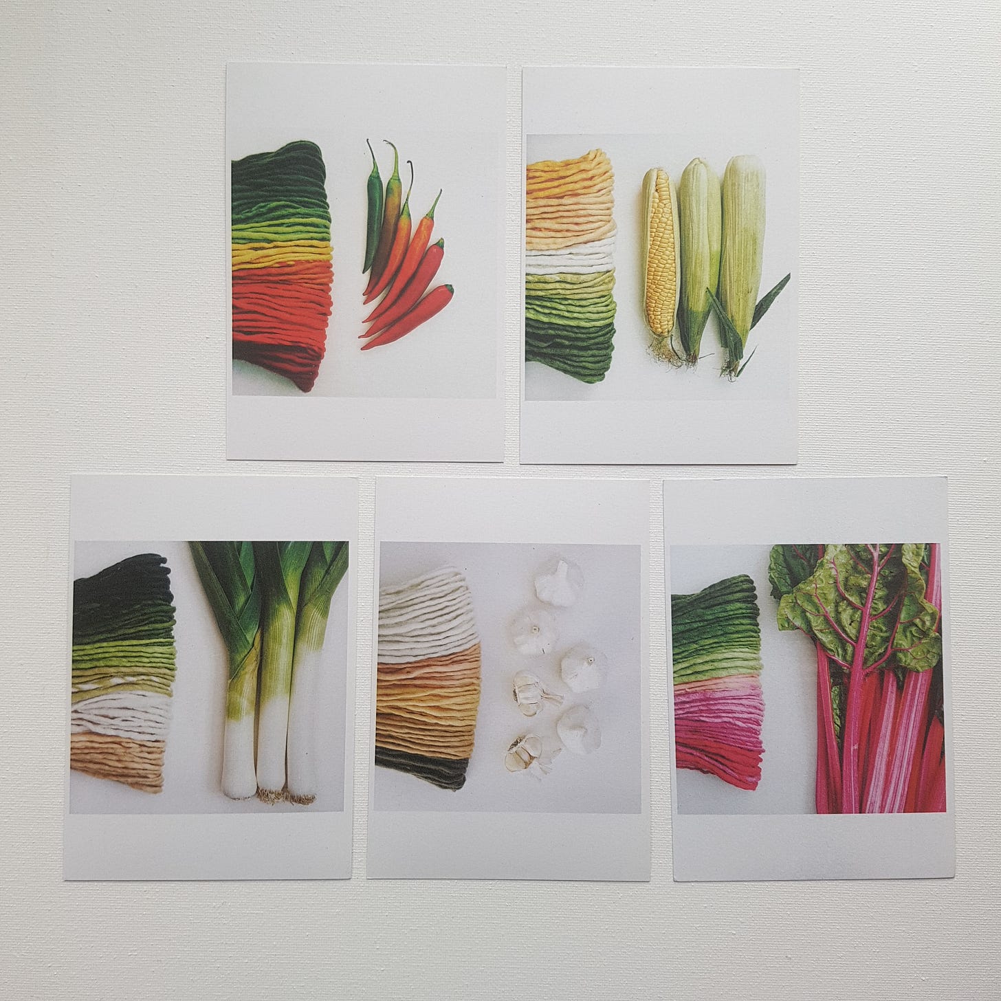 Five postcards of kitting and fruit arranged on a white desk.