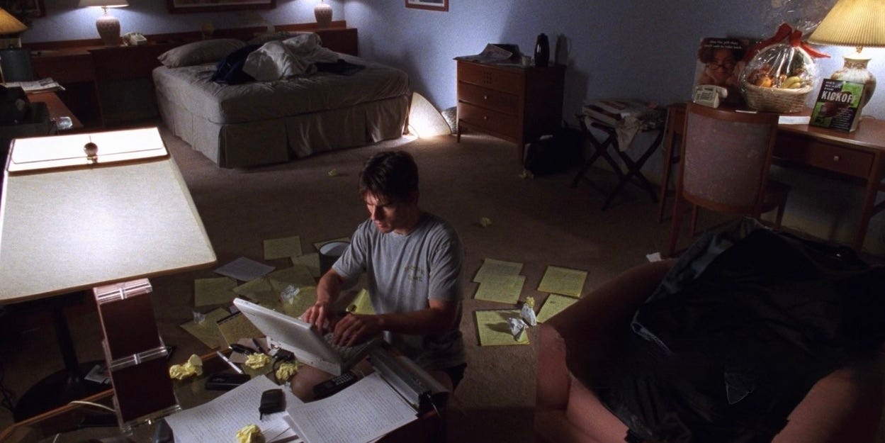 Movie still from overhead from scene in film "Jerry Maguire". Tom Cruise character sitting at a desk working at a laptop with papers all over the floor. He's working on his "Memo."
