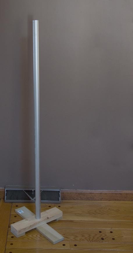 An aluminum pole stands against a plain wall