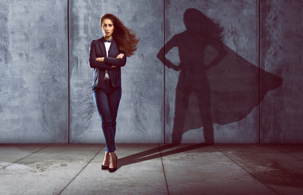 Cheesy stock photo of a woman in a blazer and high heels casting a shadow where she's a caped super woman