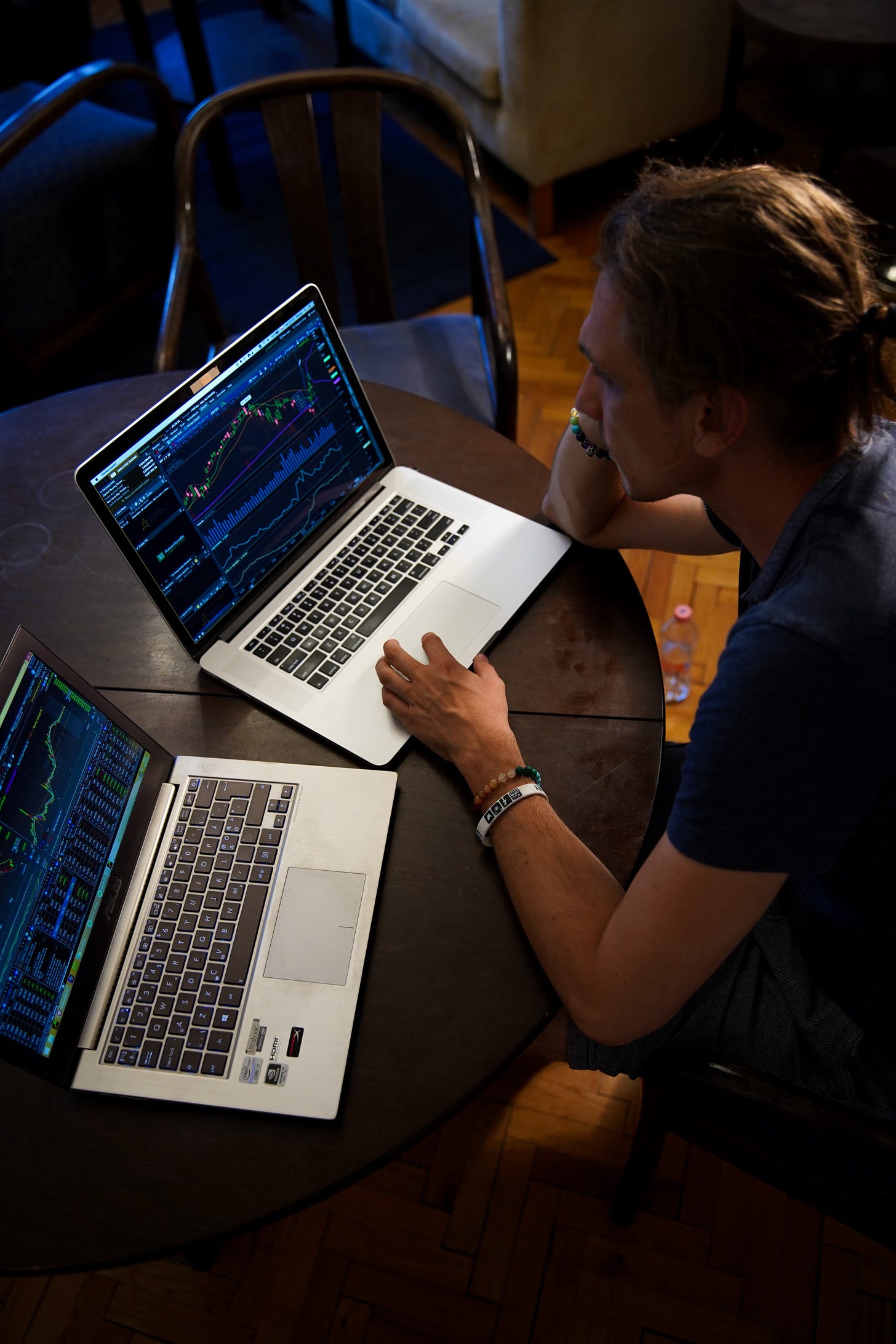 A man sitting in front of two laptops with stock charts and market data open. He’s browsing different stocks on each of the laptops.