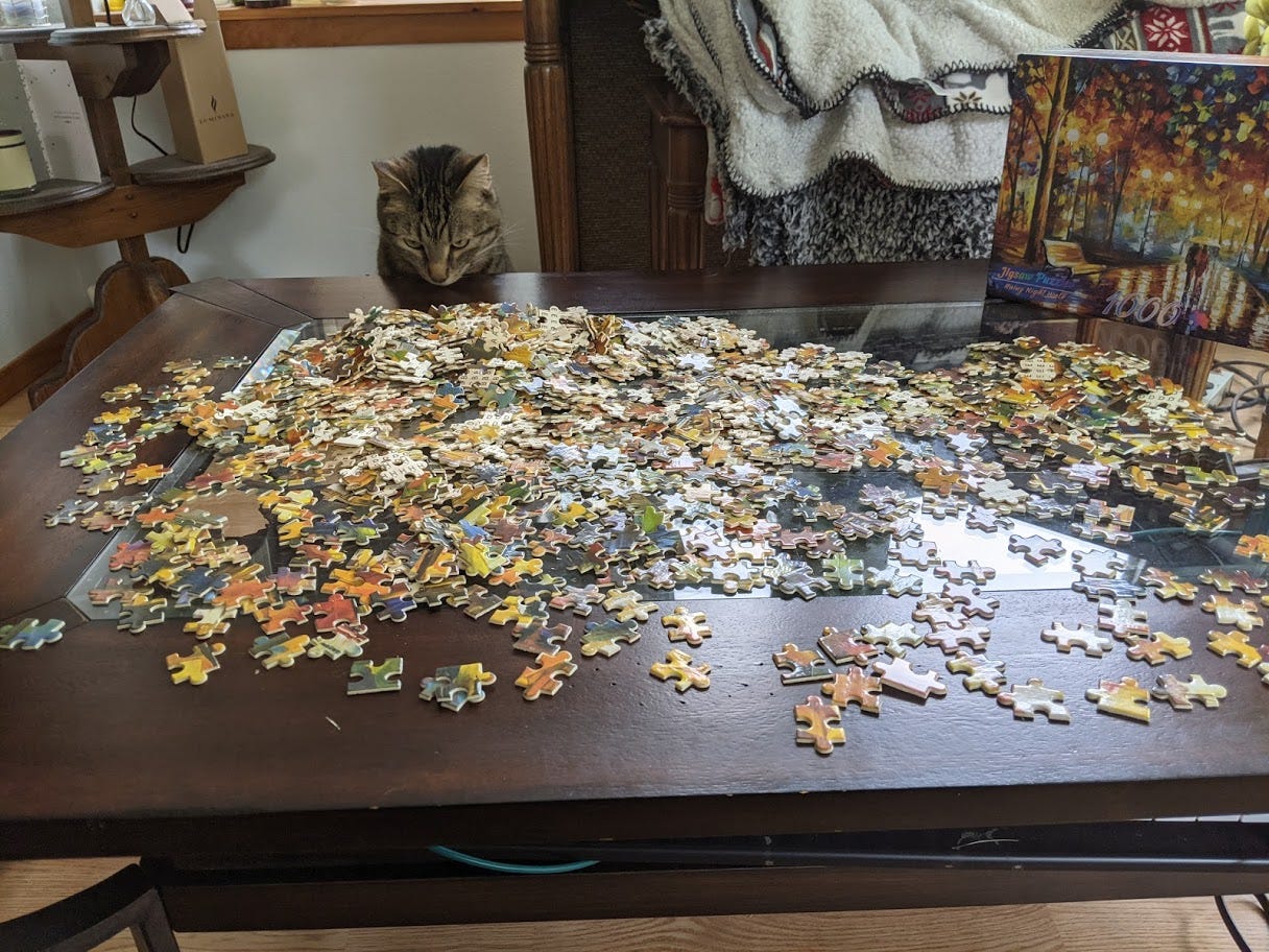 Puzzle pieces scattered on the coffee table mentioned above; a cat peeks up over the table, looking down at the puzzle pieces.