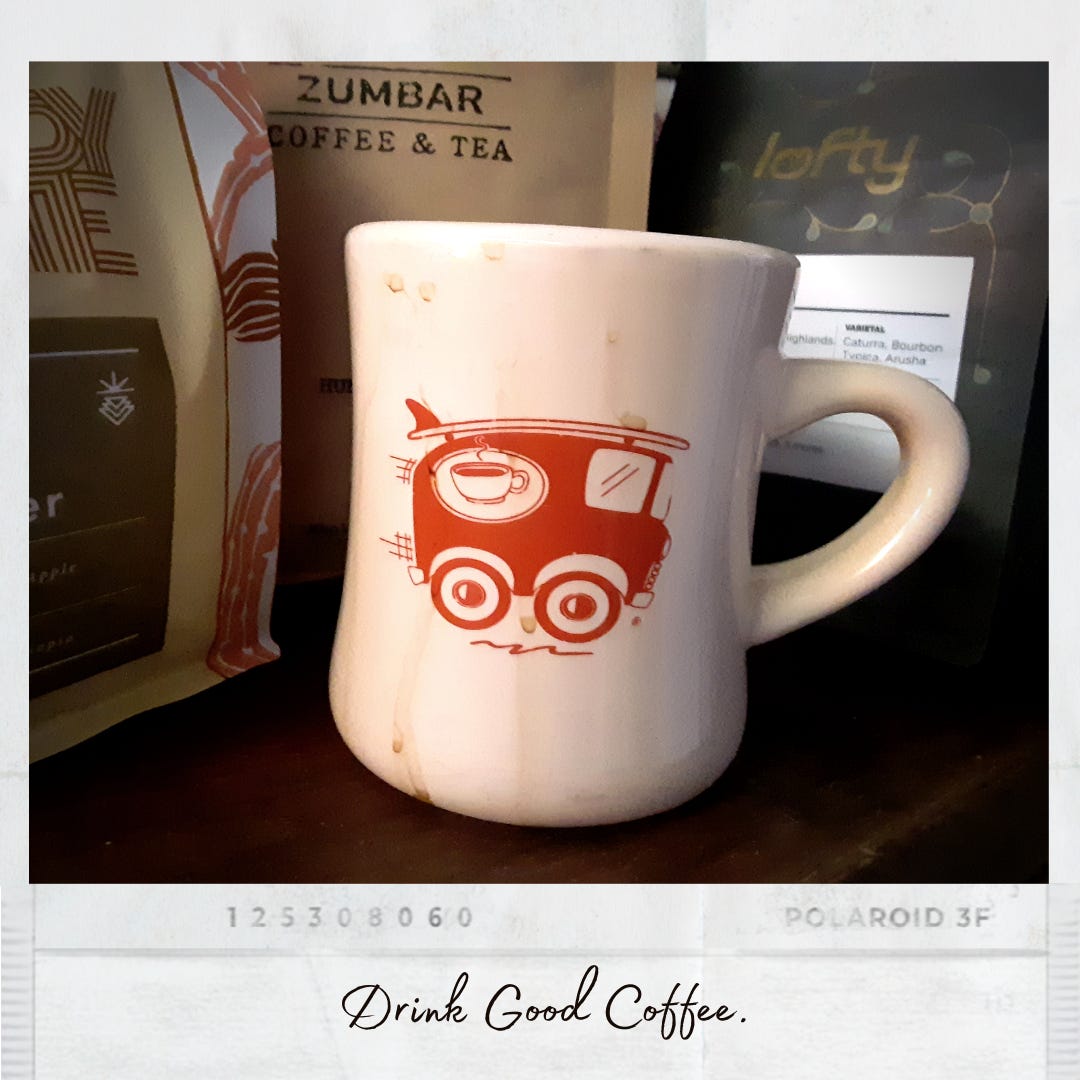 A Polaroid style film photo of a white ceramic coffee mug covered in coffee drips staining the side. An orange VW-van with a surfboard on the roof is illustrated on the side. Coffee bags from various roasters fill the background. The caption says, "Drink good coffee."