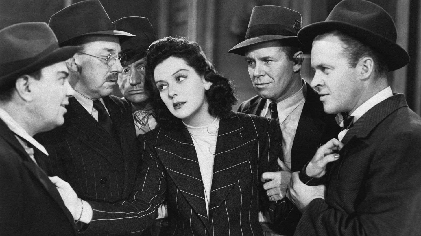 Hildy Johnson (Rosalind Russell) pushes back a group of men around her in His Girl Friday.