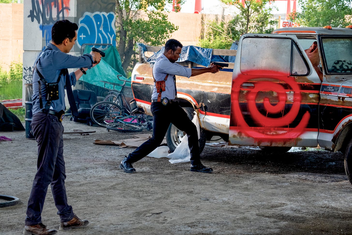 From the film "Spiral": Chris Rock plays a detective who, with his partner, have guns drawn as they approach avehicle with a red spiral spray painted on the door.