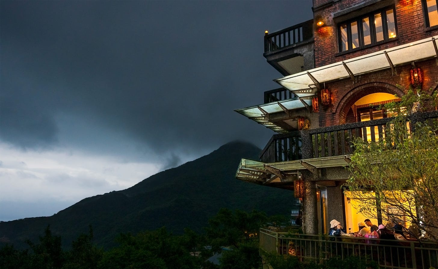 Windows glow under dark clouds hanging low over the mountains at the Artist Teahouse, one of the oldest shops in Jiufen, Taiwan